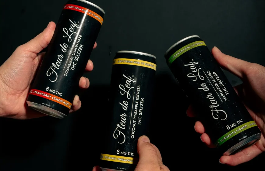 Three hands holding cans of Fleur de Leaf THC seltzers.